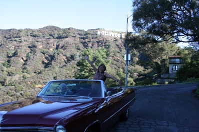 Edna Kerr standing inside classic car with Hollywood sign in background